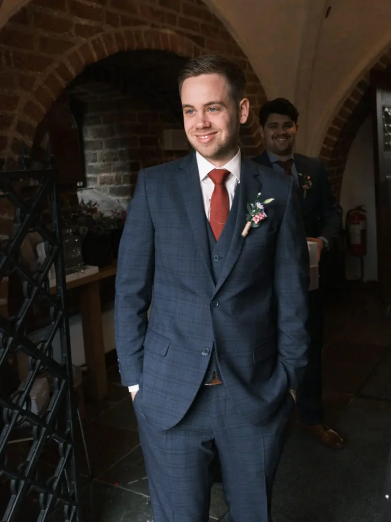 En gom smiler forventningsfuldt, stående i en buegang før bryllupsceremonien i Lyngby Kirke.