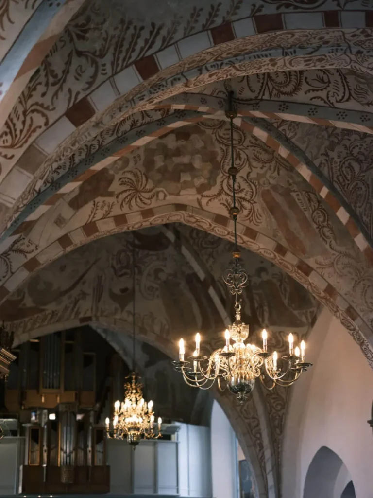 Intricate frescoes adorn the vaulted ceiling of Lyngby Church, complemented by the warm glow of chandeliers.