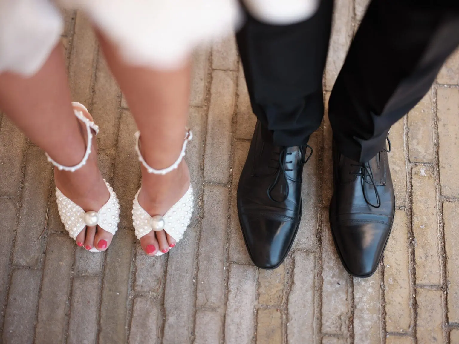 Bride's pearl-studded heels beside groom's classic black shoes, a stylish pair at Ridebanen by Christiansborg Palace.