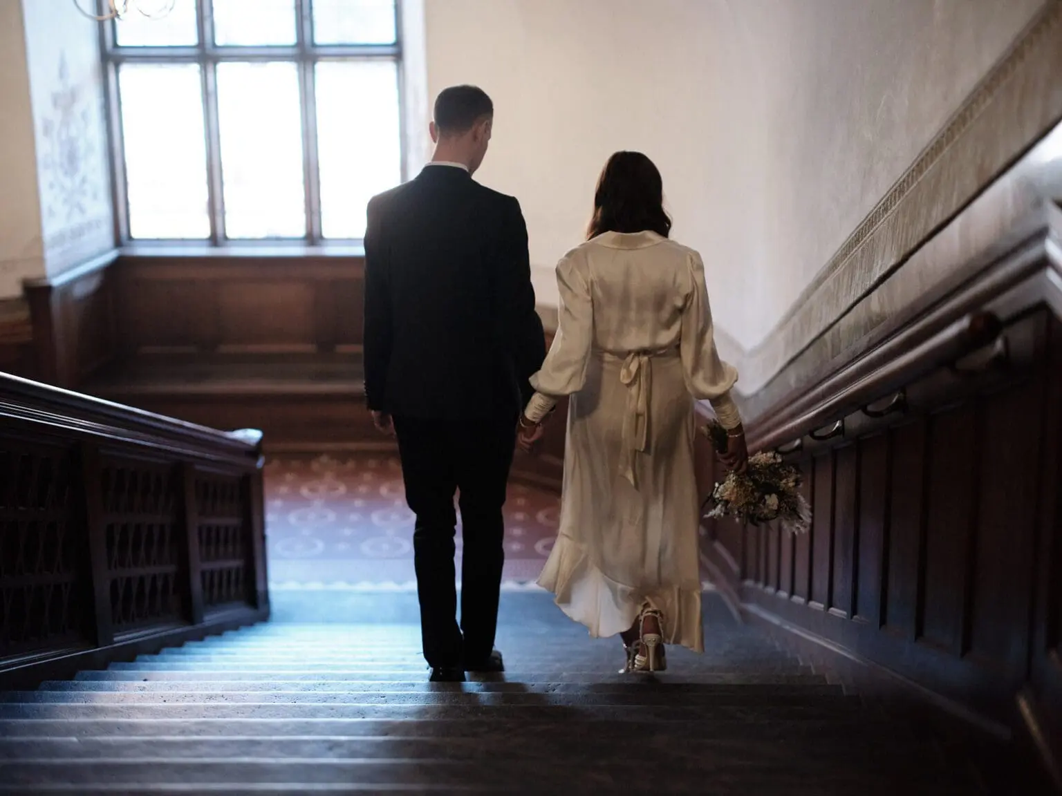 Bride and groom ascending the staircase at Copenhagen City Hall, captured from behind.