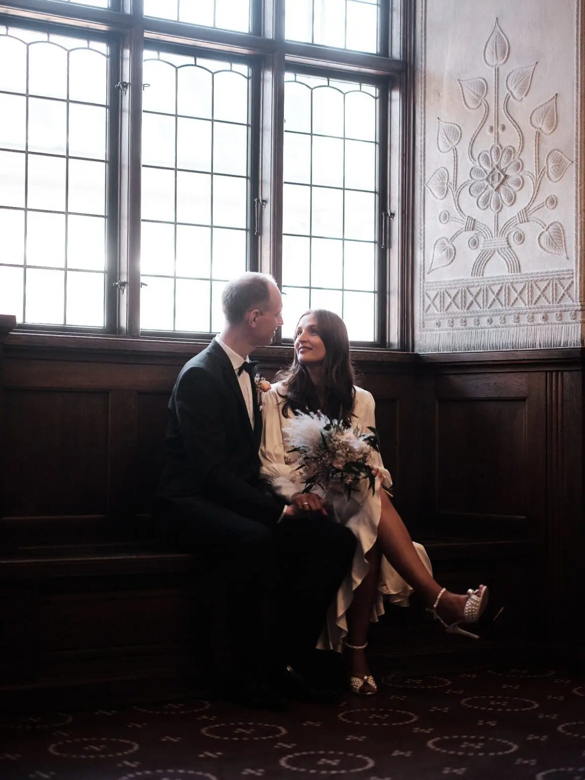 Wedding couple seated by the window at Copenhagen City Hall, sharing a moment of closeness