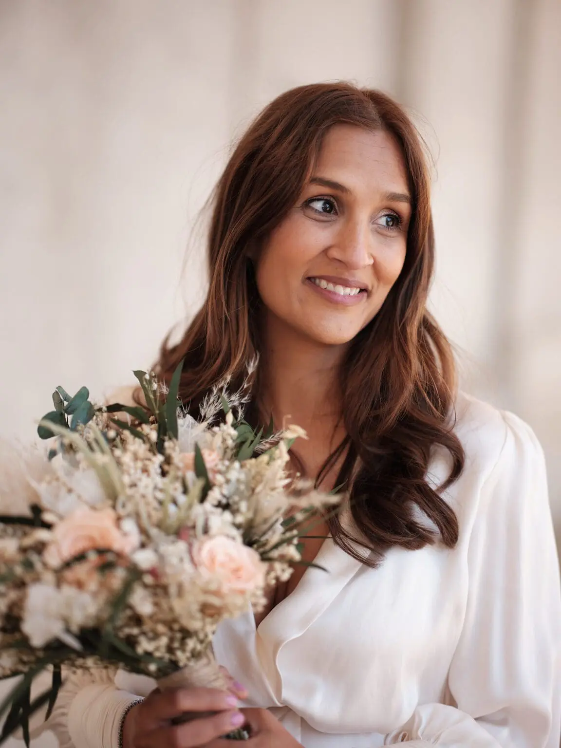 Radiant bride holding a bouquet at the Riding Grounds of Christiansborg Palace, her expression one of quiet happiness.