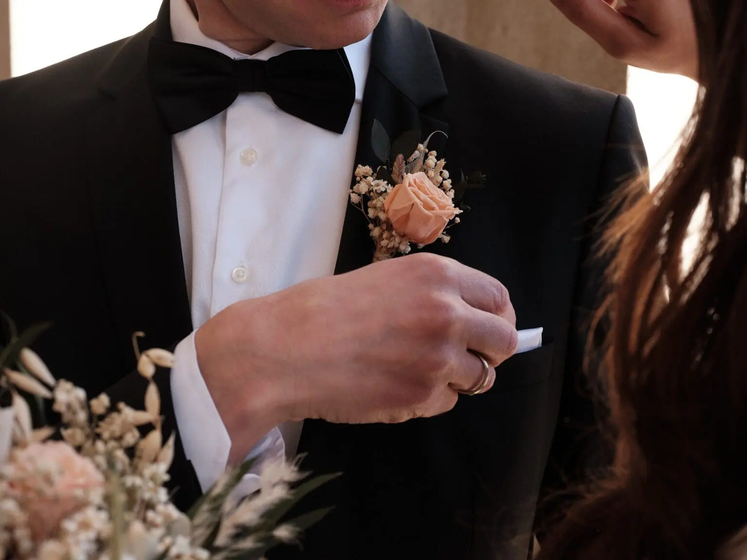 "Groom's boutonniere fastened with care, a subtle symbol of love at Copenhagen City Hall, against the backdrop of the bride's silhouette.