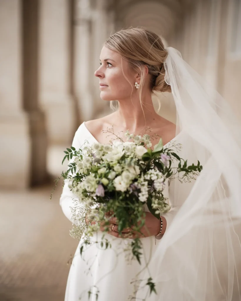 Elegant brud med slør og bryllupsbuket ser tankefuldt ud over historisk sted - Nordic Wedding
